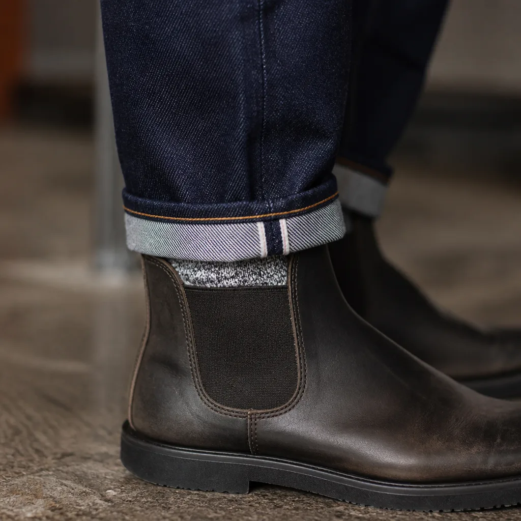 primo piano di un risvolto di denim arrotolato sopra uno stivaletto con un accenno di calzino visibile