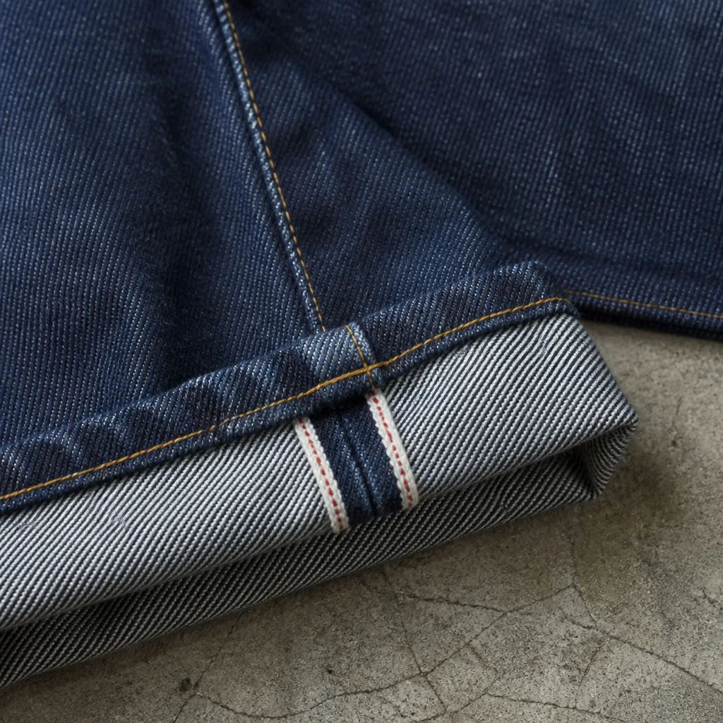 Primo piano di un orlo di jeans che mostra una cucitura ribattuta e una striscia selvedge visibile lungo l'interno gamba