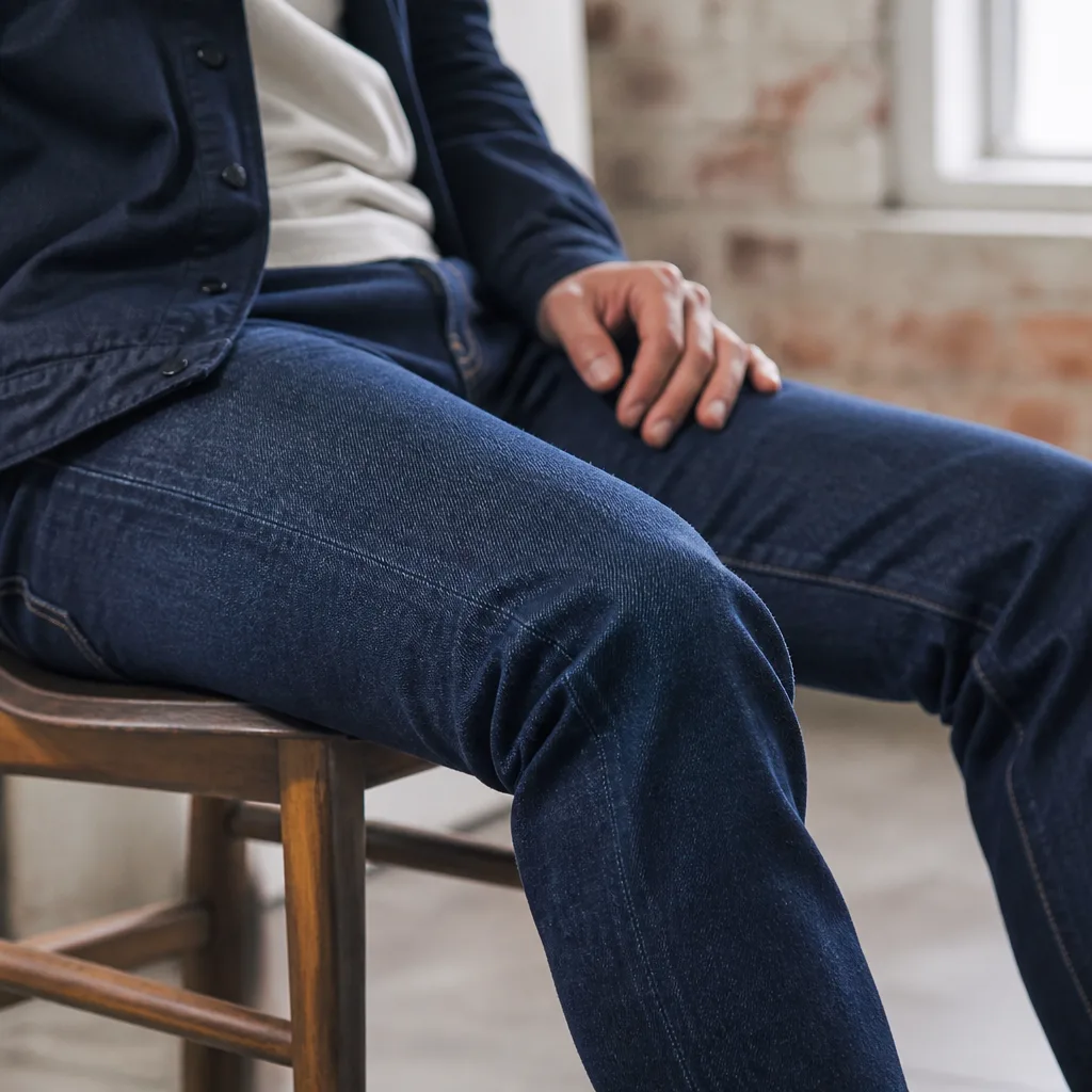 Persona seduta che indossa jeans elastici, tessuto che si flette naturalmente al ginocchio, nessun volto visibile